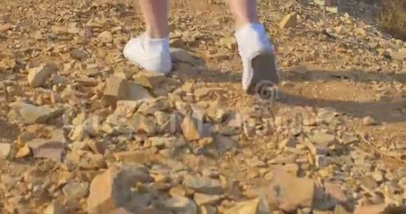 漂亮的女人穿着白色运动鞋沿着石质的地面前进在沙漠里散步视频的预览图
