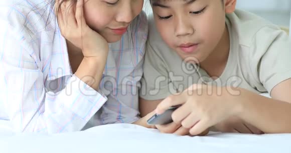 快乐亚洲家庭姐妹和兄弟在床上玩手机视频的预览图