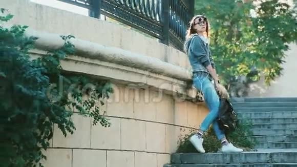 女孩带着耳机和背包靠在楼梯上的墙上漫步城市自由风采视频的预览图