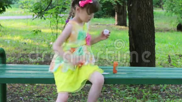 小女孩在长凳上吹泡泡夏天在绿色公园里接住视频的预览图