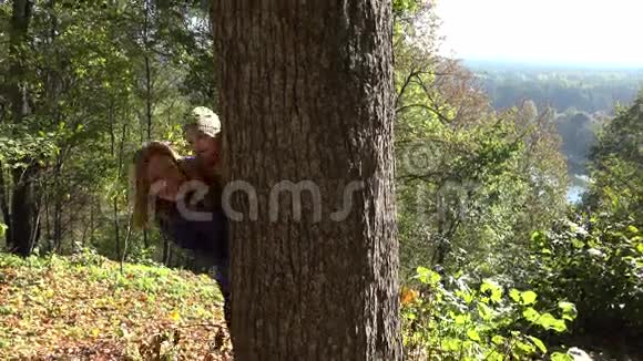 妈妈带着可爱的宝宝在秋天公园的树干上玩捉迷藏和种子4K视频的预览图