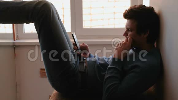 有电话的人年轻人坐在靠近窗户的阳台上用手机浏览网页视频的预览图