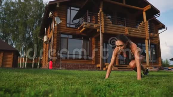一位身材苗条的年轻女子穿着黑色运动服在乡间别墅附近的草地上蹲着视频的预览图