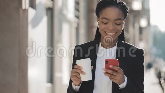 一位年轻的非洲裔美国女商人穿着西装在城市里走来走去喝着咖啡用着视频的预览图