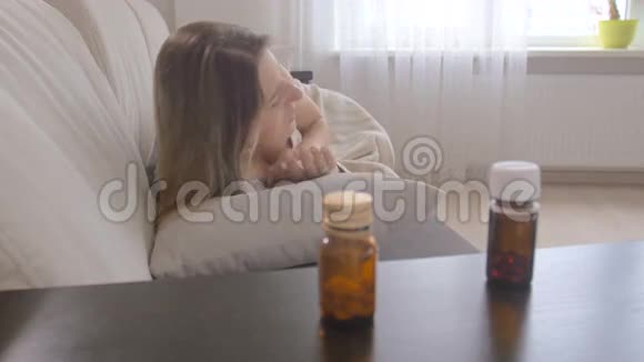 年轻的患病妇女得了流感在客厅的桌子上用瓶子吃药视频的预览图