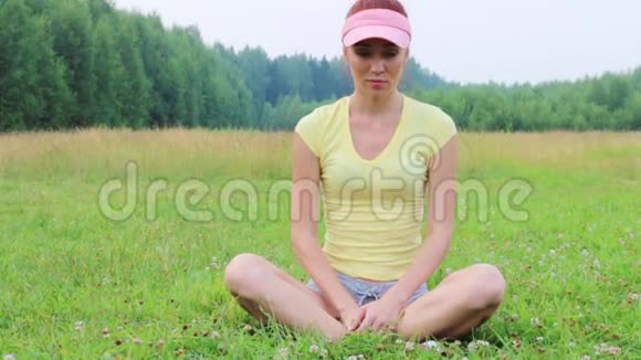 美丽的女孩坐在绿色的草地上在夏天的晚上冥想视频的预览图