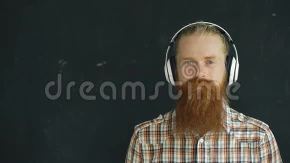 戴着耳机的留胡子年轻人的特写镜头听音乐微笑着看着镜头视频的预览图