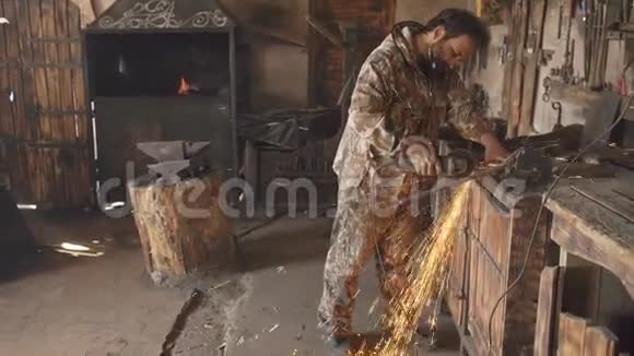 大胡子的年轻人用角磨机在铁匠作坊里加工一块金属磨出的火花四处飞舞视频的预览图