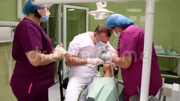 一个带着助手的牙医从一个年轻的女人身上取下牙齿视频的预览图