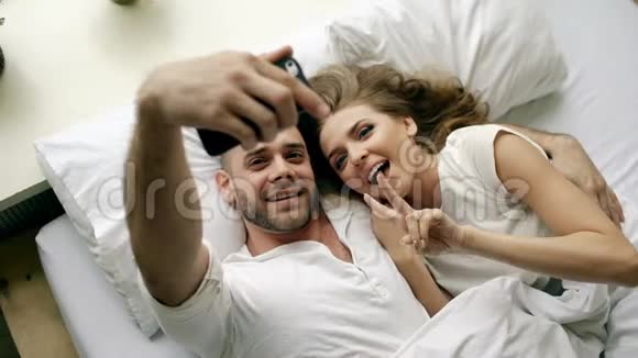 年轻美丽可爱的一对情侣在智能手机上拍照早上躺在床上接吻视频的预览图