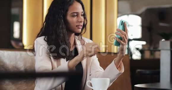 漂亮的年轻商务女性坐在舒适的咖啡馆里使用智能手机视频的预览图