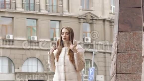 时髦的女人穿着毛茸茸的外套走着跑道在街上摆姿势慢慢地视频的预览图