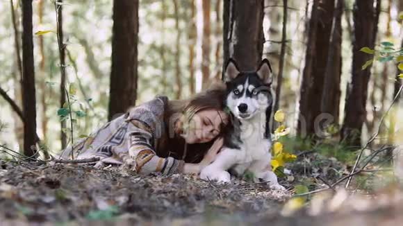 一位年轻的自然女人躺在草地上拥抱着她那只看起来像狼的狗视频的预览图