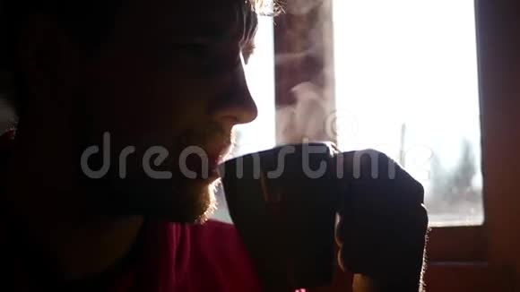 一个长着浓密胡须的男人坐在窗户对面喝着美味的热黑咖啡动作缓慢视频的预览图