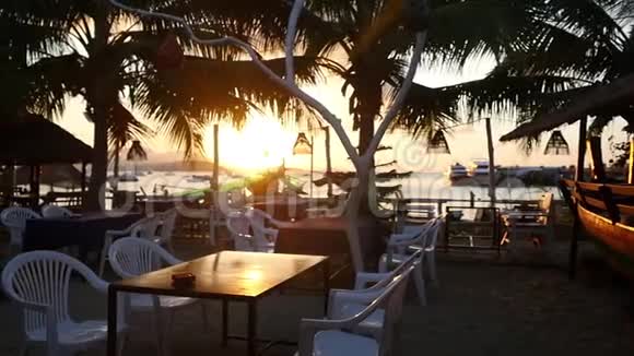 空的海滨餐厅有木制长凳和桌子在令人惊叹的日落与棕榈树慢动作1920x1080视频的预览图