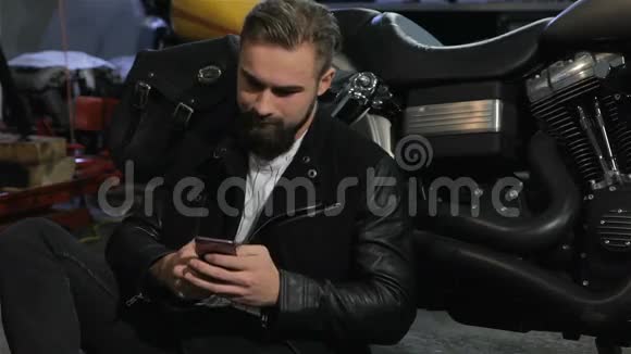 男摩托车手在摩托车车间的直升机旁用手机视频的预览图