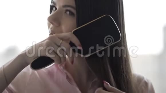穿着粉红色衬衫的布鲁内特女孩正在梳理她美丽的长发梳子视频的预览图