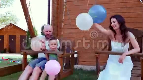 一家人骑在秋千上一个幸福的家庭的肖像爸爸妈妈和儿子玩得很开心手里拿着气球笑着视频的预览图
