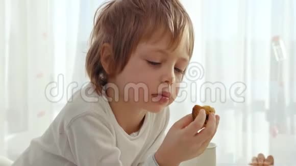 男孩在现代厨房吃早餐男孩吃带牛奶的饼干厨房里的白色桌子碗在桌子上视频的预览图