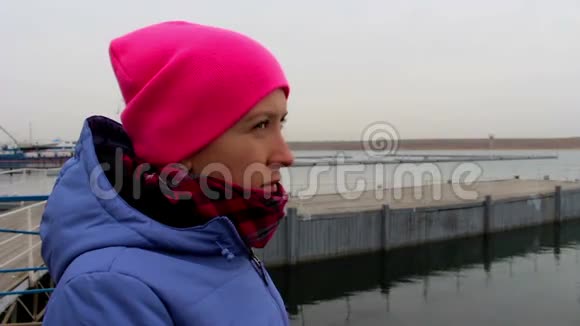 一个女孩戴着粉红色帽子在码头上的肖像在秋天寒冷的阴天视频的预览图