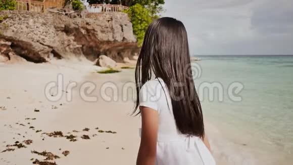 一个迷人而快乐的菲律宾少女穿着白色的夏装正沿着靠近岩石的热带海滩奔跑视频的预览图