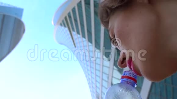 女孩喝水从瓶子对摩天大楼4K特写视频从下面的视图视频的预览图