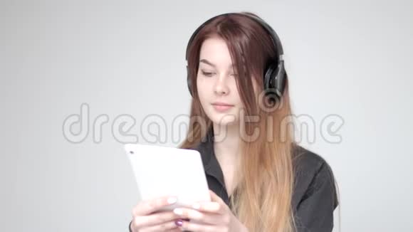戴着耳机的漂亮年轻女人在白色背景下玩平板电脑视频的预览图