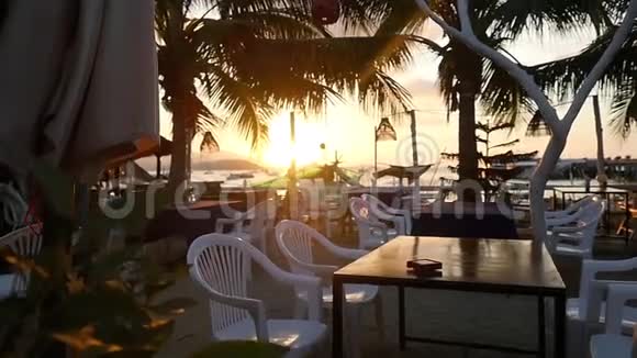 空的海滨餐厅在美丽的日落和棕榈树上有木制长凳和桌子慢动作1920x1080视频的预览图