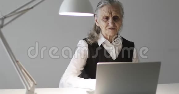 一个皱纹很深的老妇人在笔记本电脑上工作视频的预览图