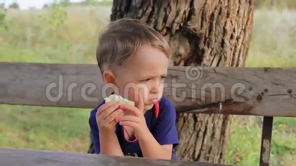 男孩坐在户外的长凳上吃饭视频的预览图