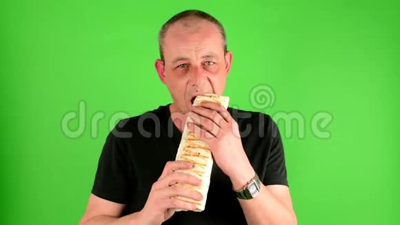 成熟的中年男人一个成熟的男人在绿色屏幕前吃快餐烤肉串的肖像也叫陀螺视频的预览图