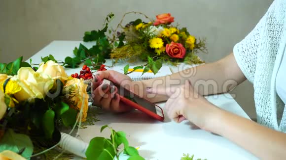 花艺设计师女孩的手特写镜头她用手机在餐桌上与鲜花通信视频的预览图