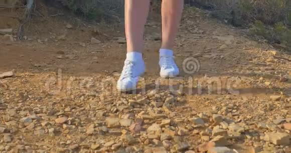 漂亮的女人穿着白色运动鞋沿着石质的地面前进在沙漠里散步视频的预览图