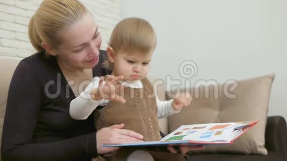 妈妈读他的小女儿坐在客厅沙发上的书视频的预览图