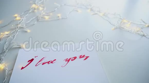 在白色的纸上在桌上闪烁着我爱你的温柔的旗舰刻字特写视频的预览图