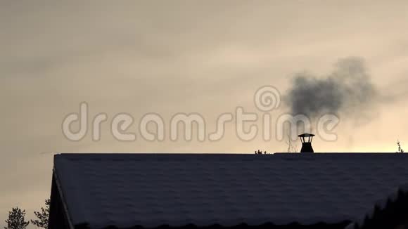 鸟儿在冬夜的日落中飞翔烟囱里冒出的烟在白雪覆盖的屋顶上视频的预览图