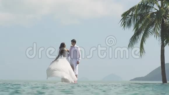 新娘正在玩她的白色婚纱年轻漂亮的男人和女人在海滩上互相拥抱快乐视频的预览图