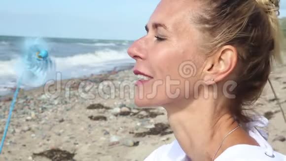 金发女人坐在沙滩上拿着一个风车视频的预览图