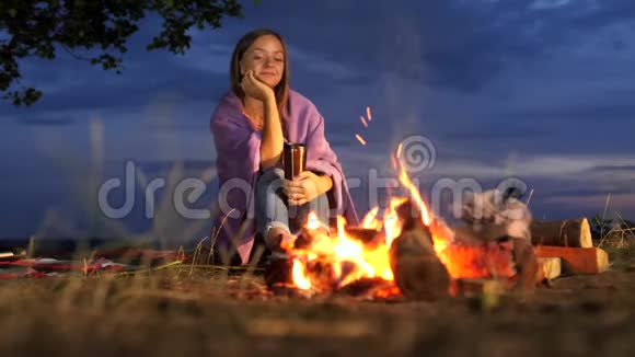 永女坐在篝火旁喝着热饮料看着篝火视频的预览图