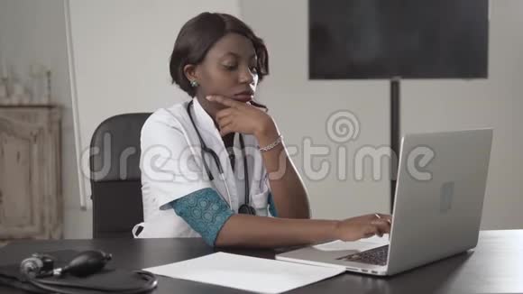 黑人女医生坐在办公桌前看镜头非裔美国人护士在柜子里的笔记本电脑上工作现代视频的预览图
