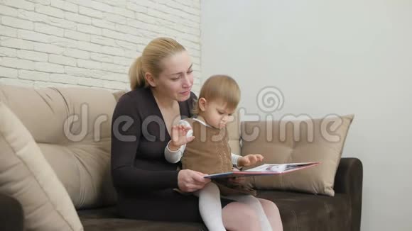 妈妈读他的小女儿坐在客厅沙发上的书视频的预览图