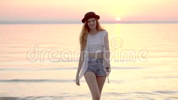 戴着帽子的漂亮金发女人在海上享受夏日假期金色的夕阳视频的预览图