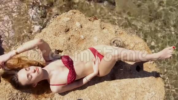 穿红色泳衣的苗条女士在岩石上日光浴视频的预览图