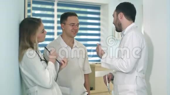 男医生拿着药片在医院大厅里和另外两名医生交谈视频的预览图