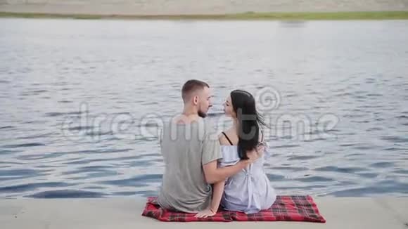一对相爱的夫妇坐在河边亲吻和拥抱视频的预览图