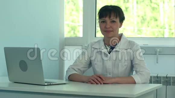 女医生带着笔记本电脑在办公桌上工作对着相机微笑视频的预览图