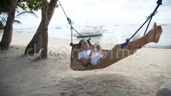 沙滩上拿着平板电脑吊床的女孩视频的预览图