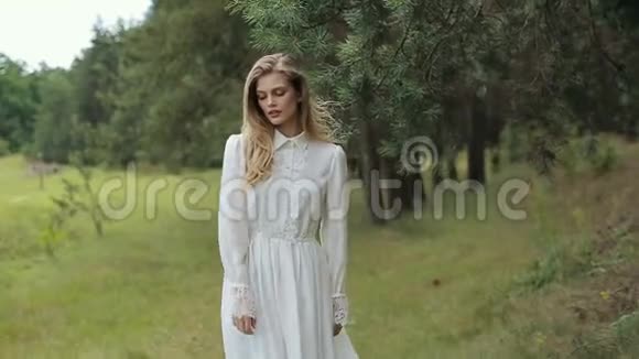 穿着白色裙子的漂亮女孩在绿林附近的镜头前摆姿势视频的预览图