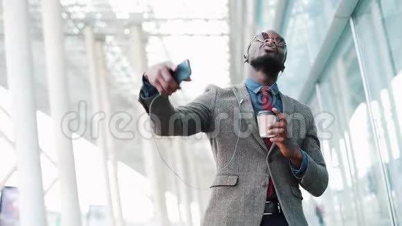 快乐的非裔美国商人在智能手机上听耳机里的音乐走在办公室外面很有趣视频的预览图