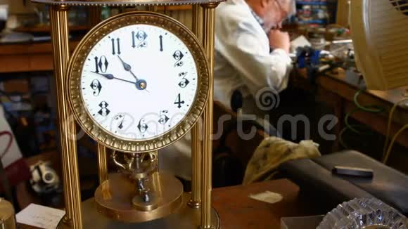 老式扭摆钟摆在桌子上而钟表学家则在后台工作视频的预览图